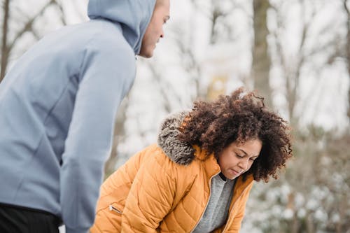 Free Crop black personal coach standing near exhausted African American female in warm outerwear during training in winter time om blurred background Stock Photo