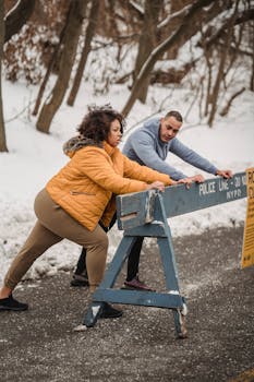 Full body of sporty African American couple leaning on wooden fence while doing stretching exercises before workout in winter time