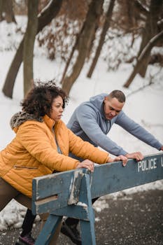 Couple in activewear stretching against a barrier in a snowy park, winter fitness concept.