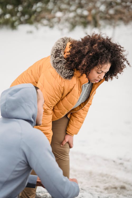 Unrecognizable trainer squatting near tired black woman in winter park