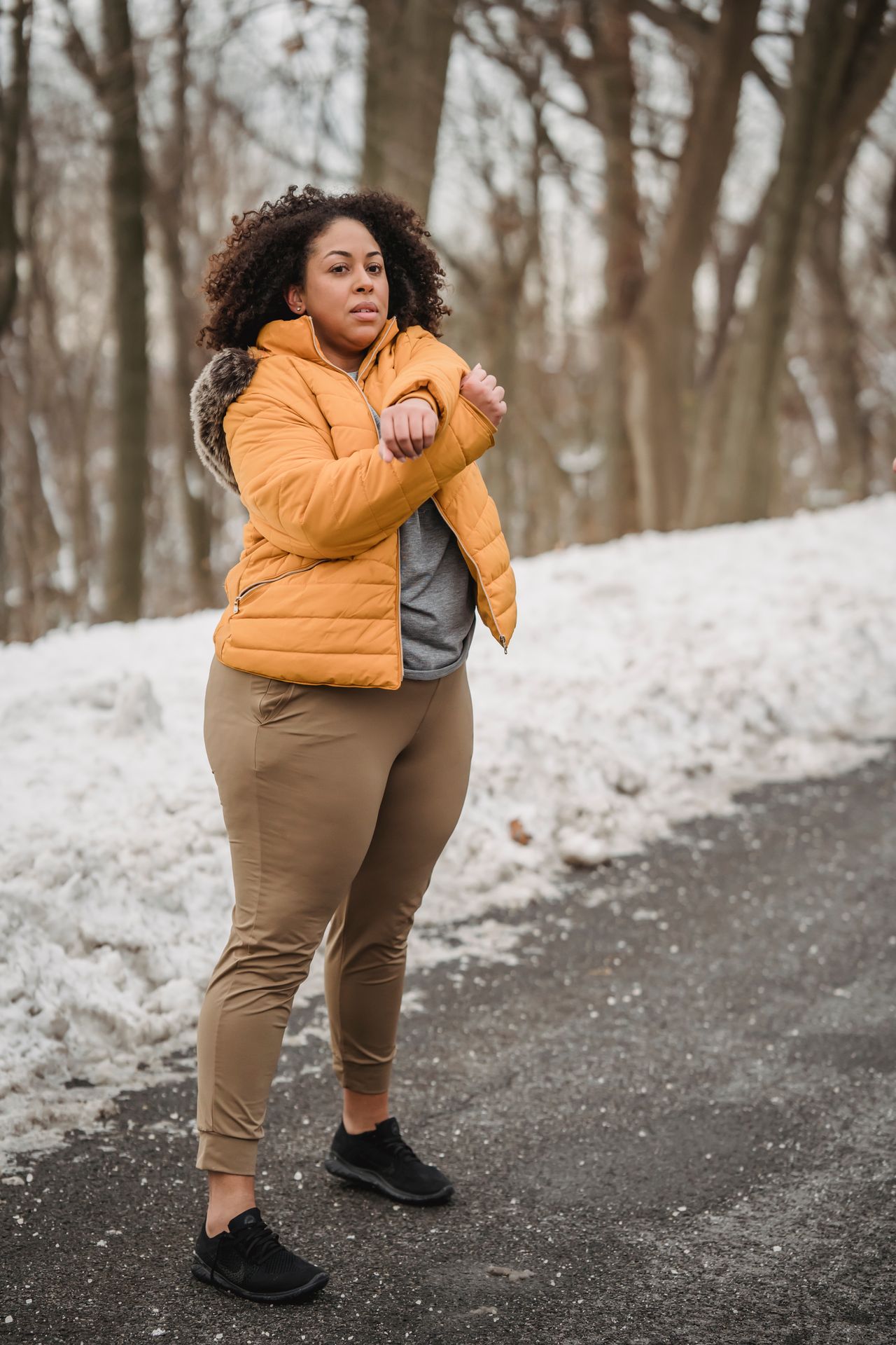 Plus-size woman in a mustard puffer jacket stretching in the snow