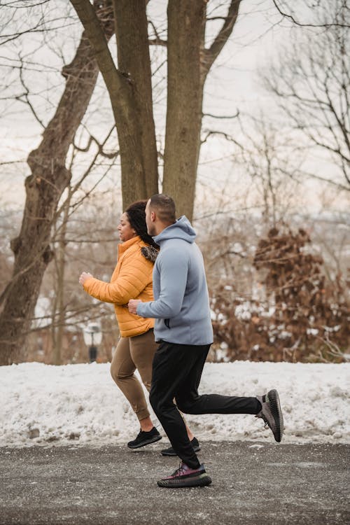 Full body side view of plus size African American female running with black coach in winter park with trees during training