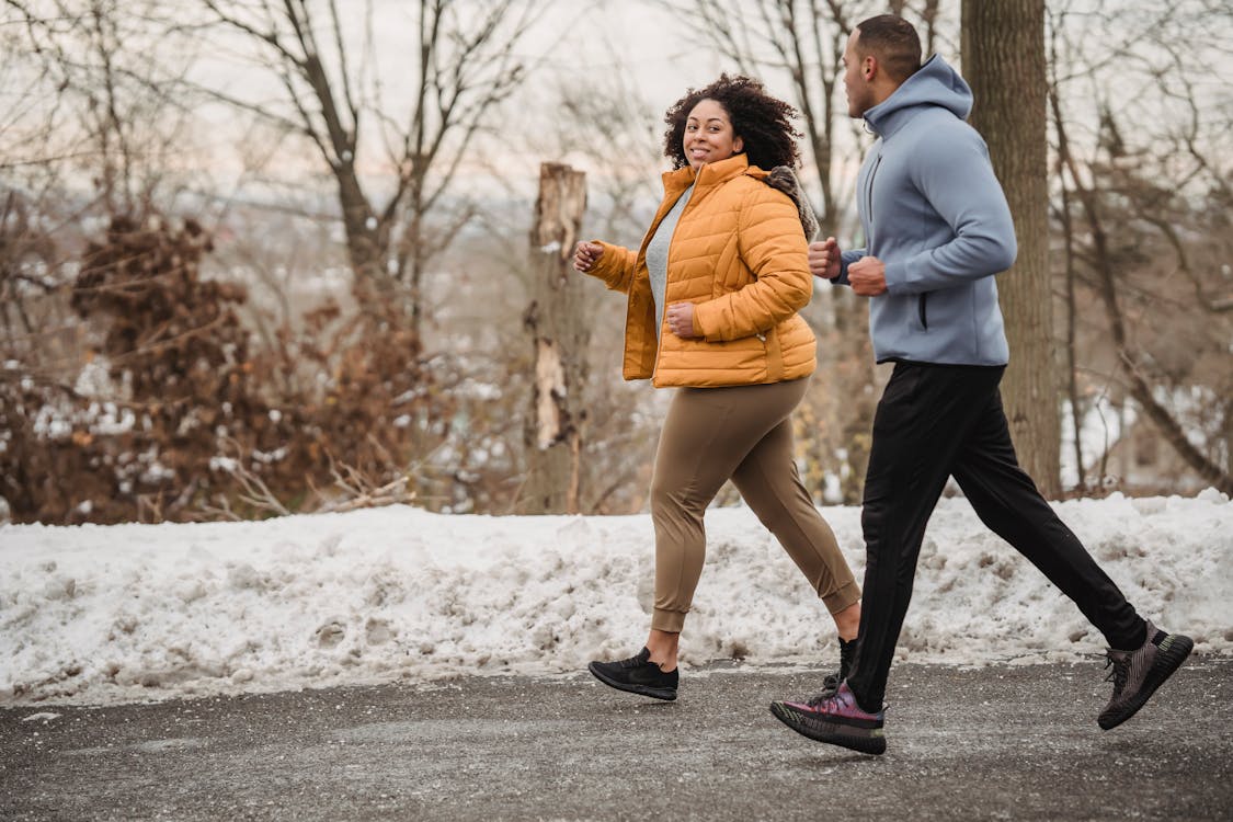 Free Full body of positive curvy African American woman and black coach looking at each other while jogging on asphalt walkway in winter time Stock Photo