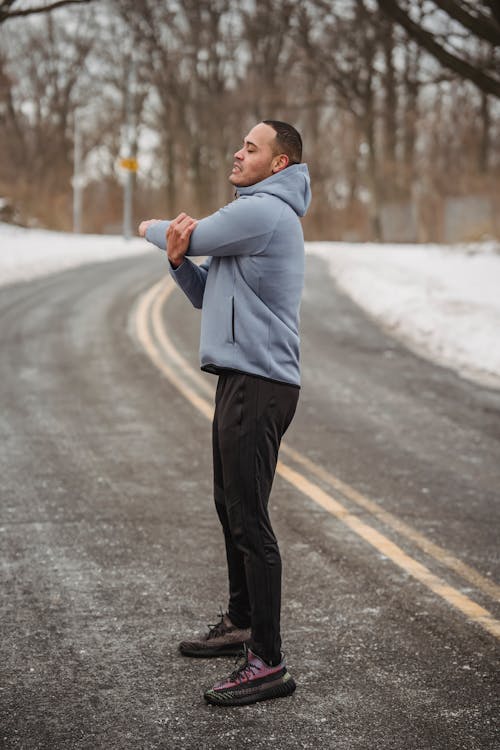 Full body side view of African American male in sportswear warming up while standing on asphalt walkway during training in winter time