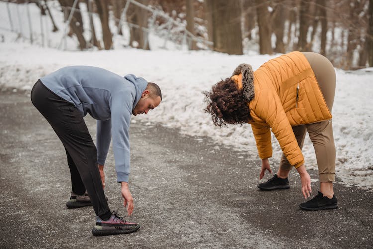 Sportive Black Couple Warming Up In Snowy Park With Trees