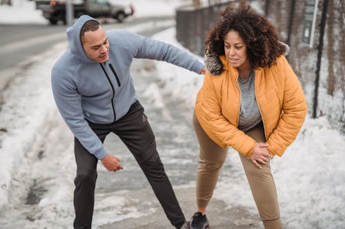 Free African American coach in sportswear helping plus size black female to warm up while standing on snowy pathway during training in winter time Stock Photo