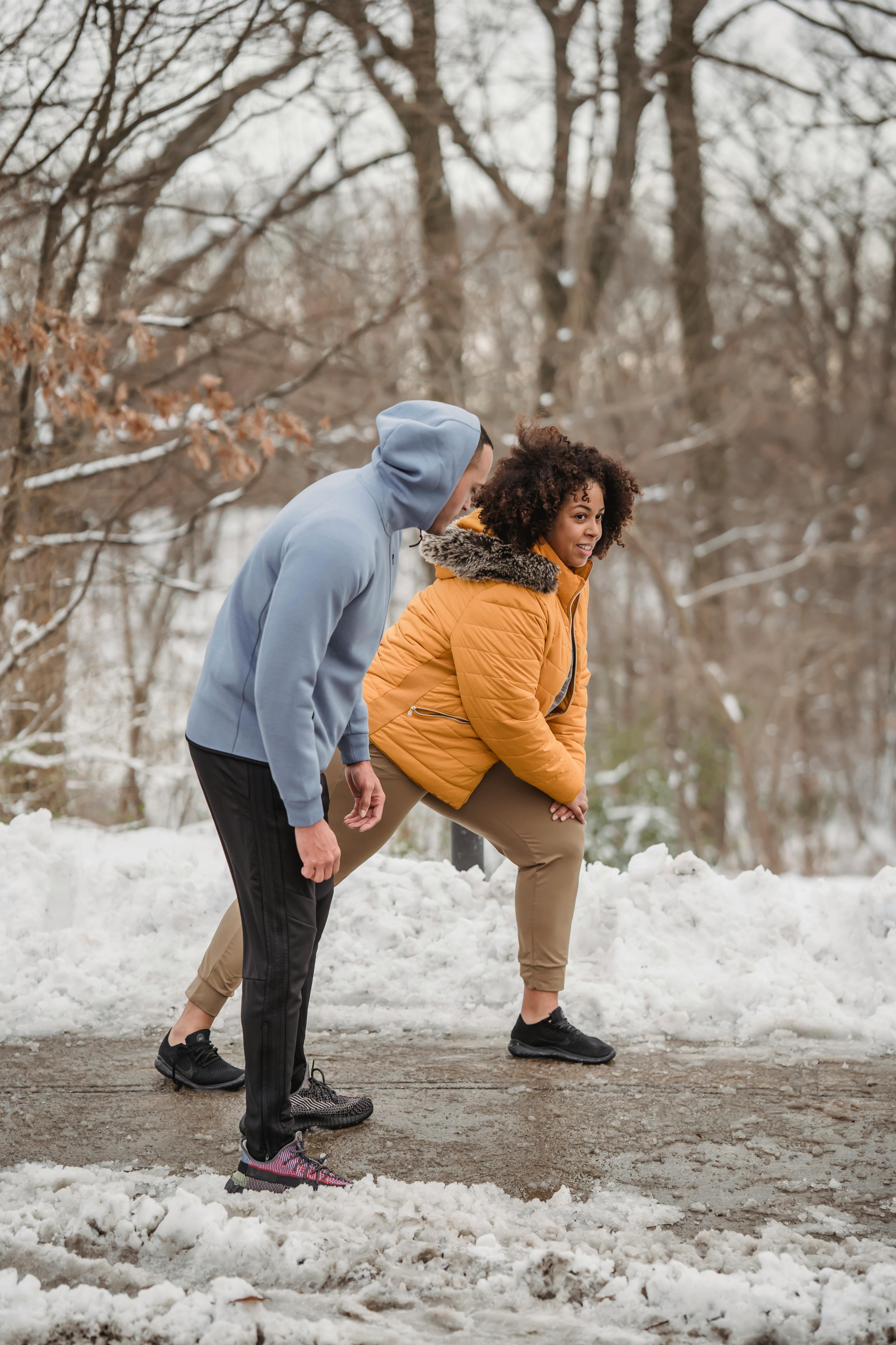 trainer and black woman stretching in winter forest