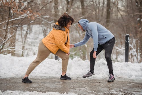 Professional instructor helping African American female doing exercises on frozen path of winter park