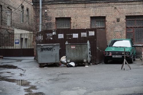Free A gritty urban alley featuring garbage bins, scattered litter, and an old parked car. Stock Photo