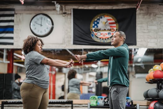 Side view of focused African American female and experienced instructor stretching hands in gym