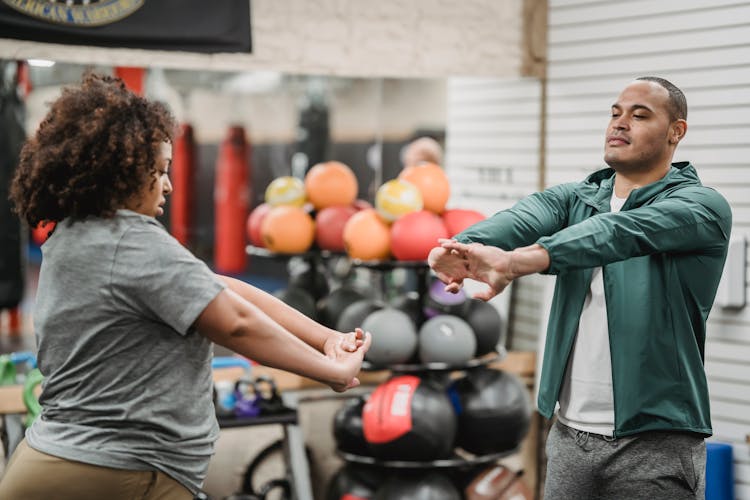 Black Woman Warming Up With Trainer In Gym