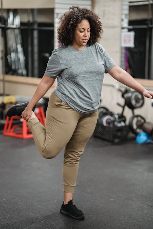Full body of concentrated plump African American female warming up on blurred background of gym