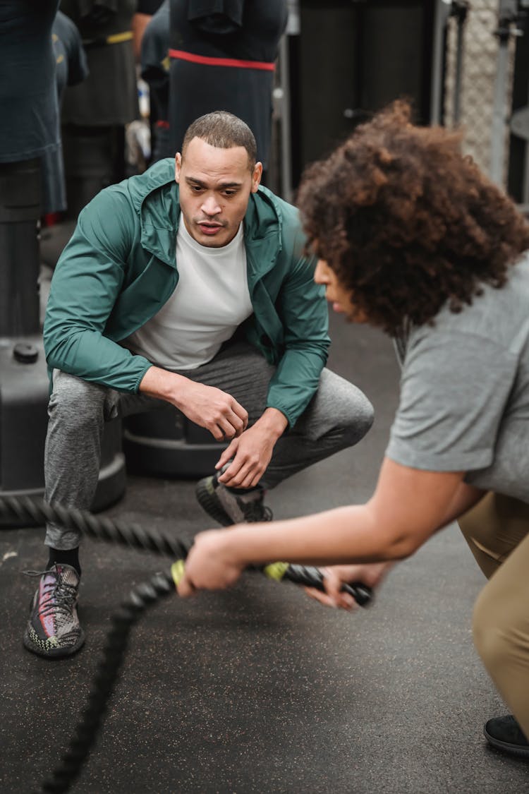 Ethnic Woman Exercising With Battling Ropes Near Male Trainer