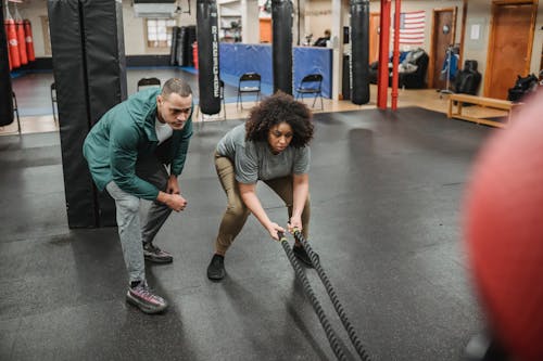 Free Full body black female in sportswear exercising with battle ropes near professional male instructor in modern gym Stock Photo