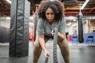 Determined black woman exercising with battle ropes in gym