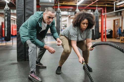 Free Determined black woman exercising with battle ropes near male coach Stock Photo