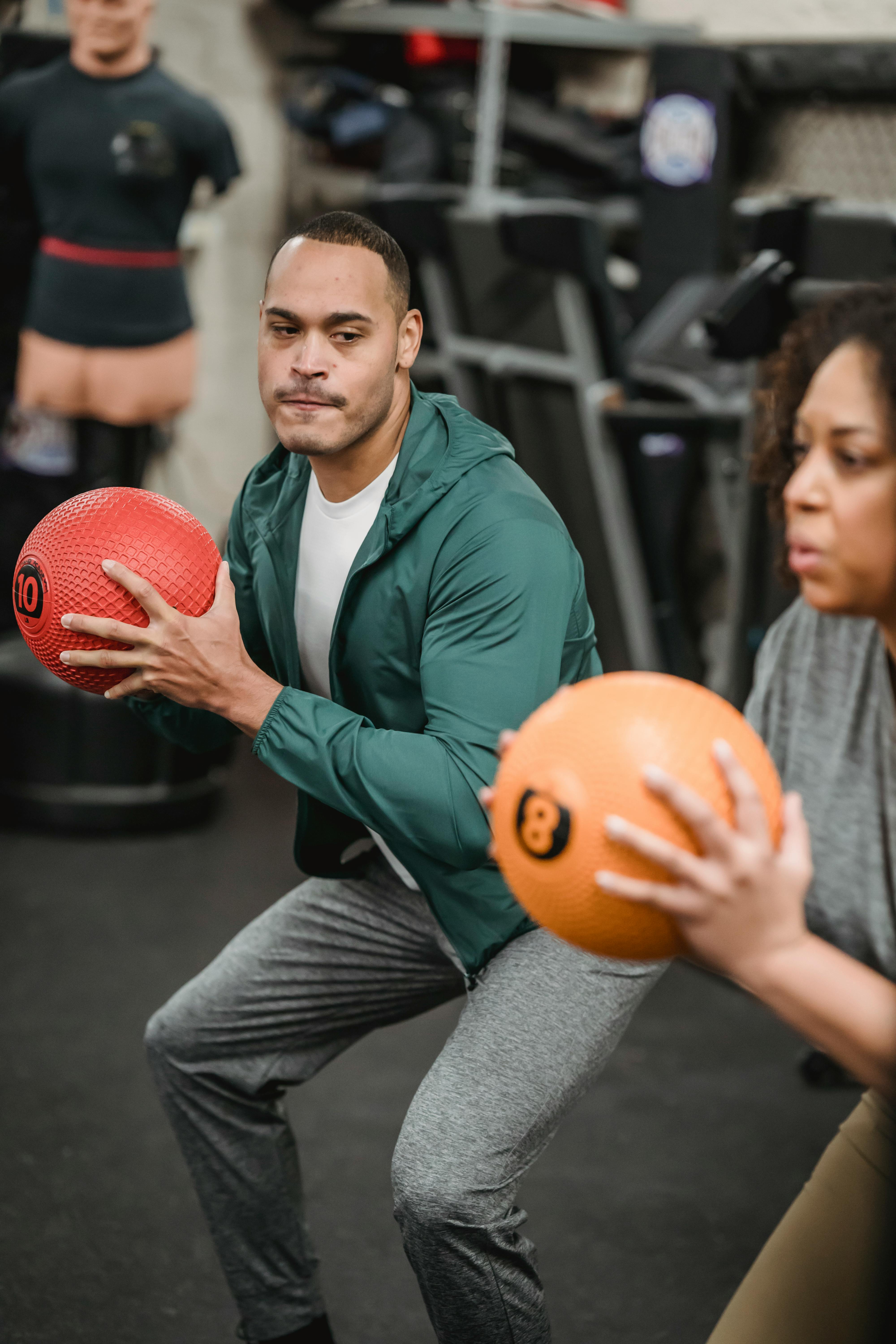 focused multiethnic athletes doing squats with medicine balls in gym