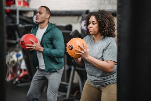 Two adults engaging in a workout with medicine balls in an indoor gym setting.