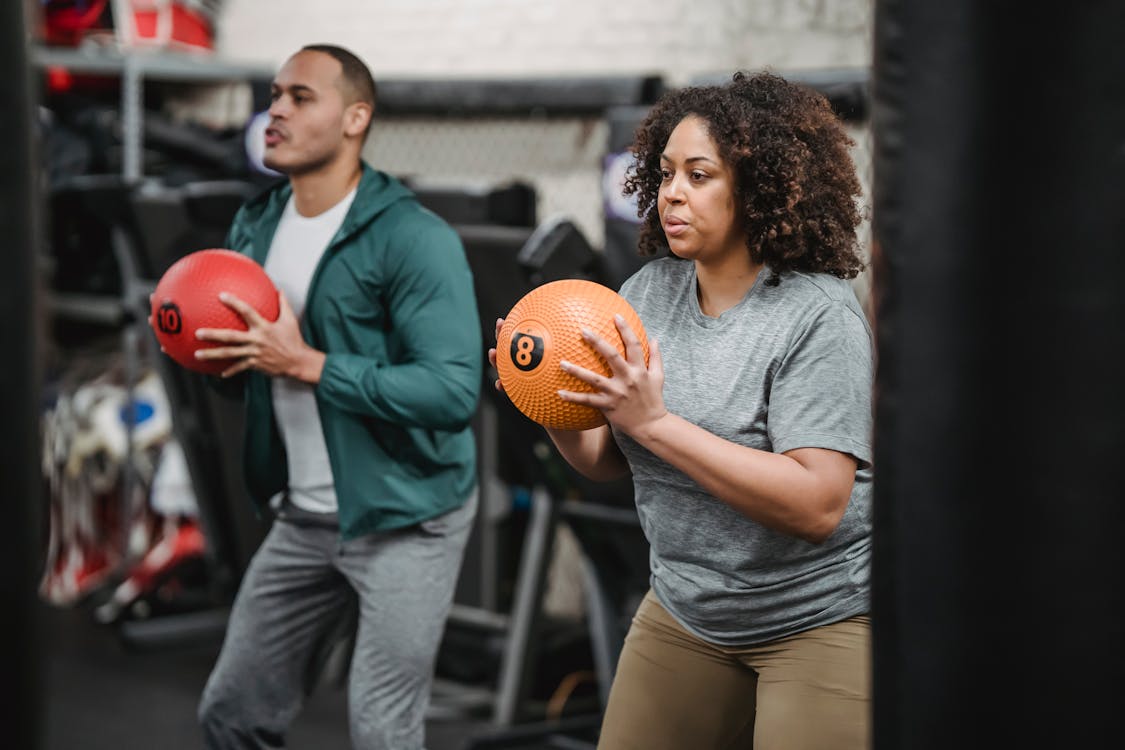 Free Concentrated young diverse trainer and athlete exercising with medicine balls in gym Stock Photo