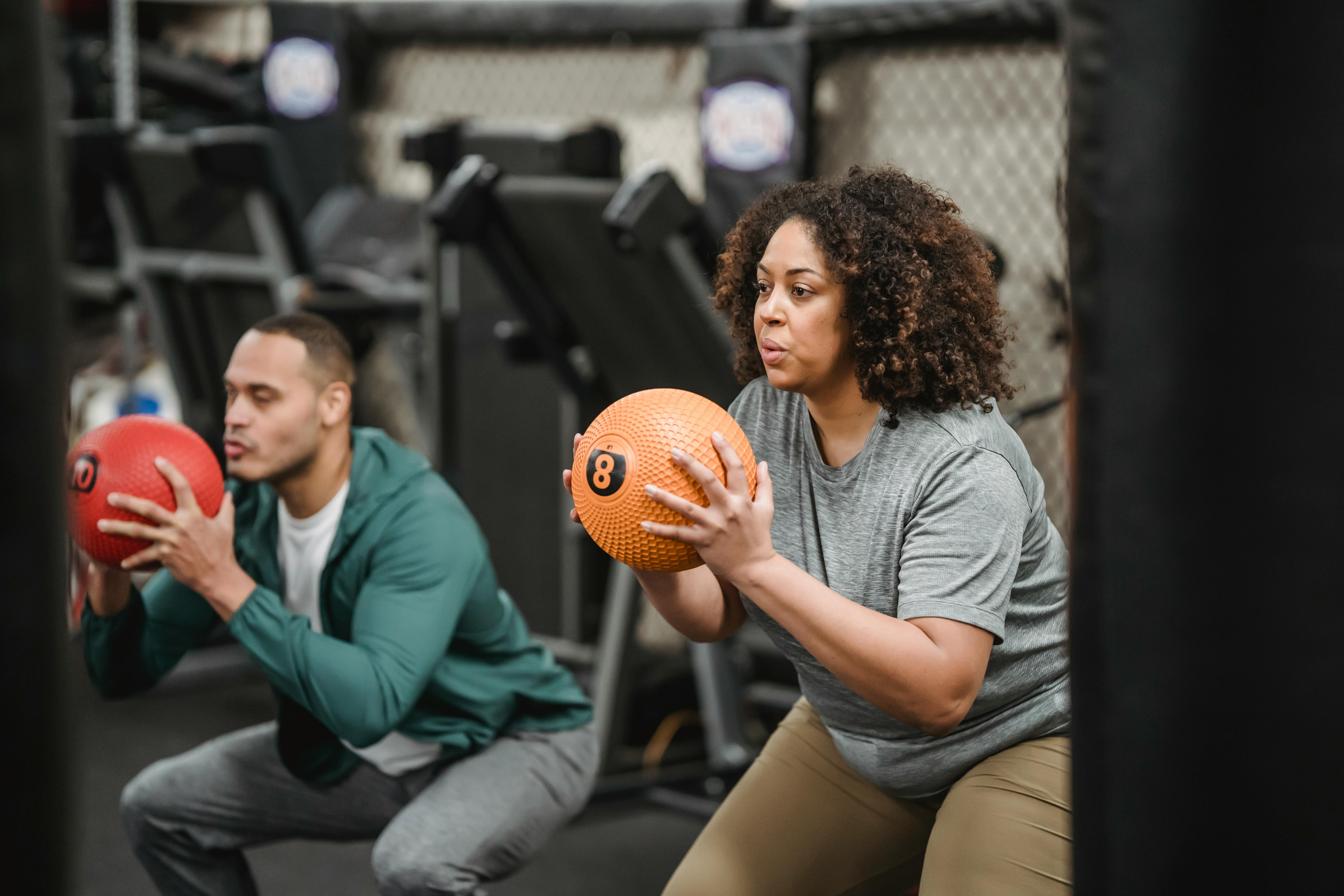 Active diverse man and woman exercising with balls in modern gym