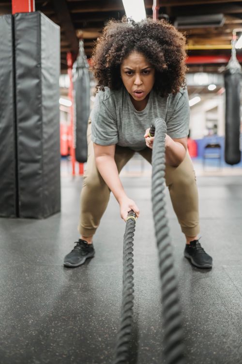 Free Full body of serious young African American plus size female in sportswear exercising with battle ropes in gym Stock Photo