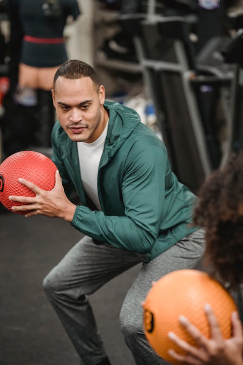 Ethnic man with weight ball doing squats with anonymous black woman