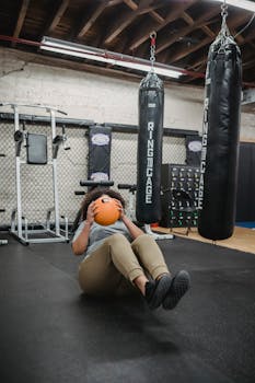 African American woman exercising indoors with a medicine ball in a gym.