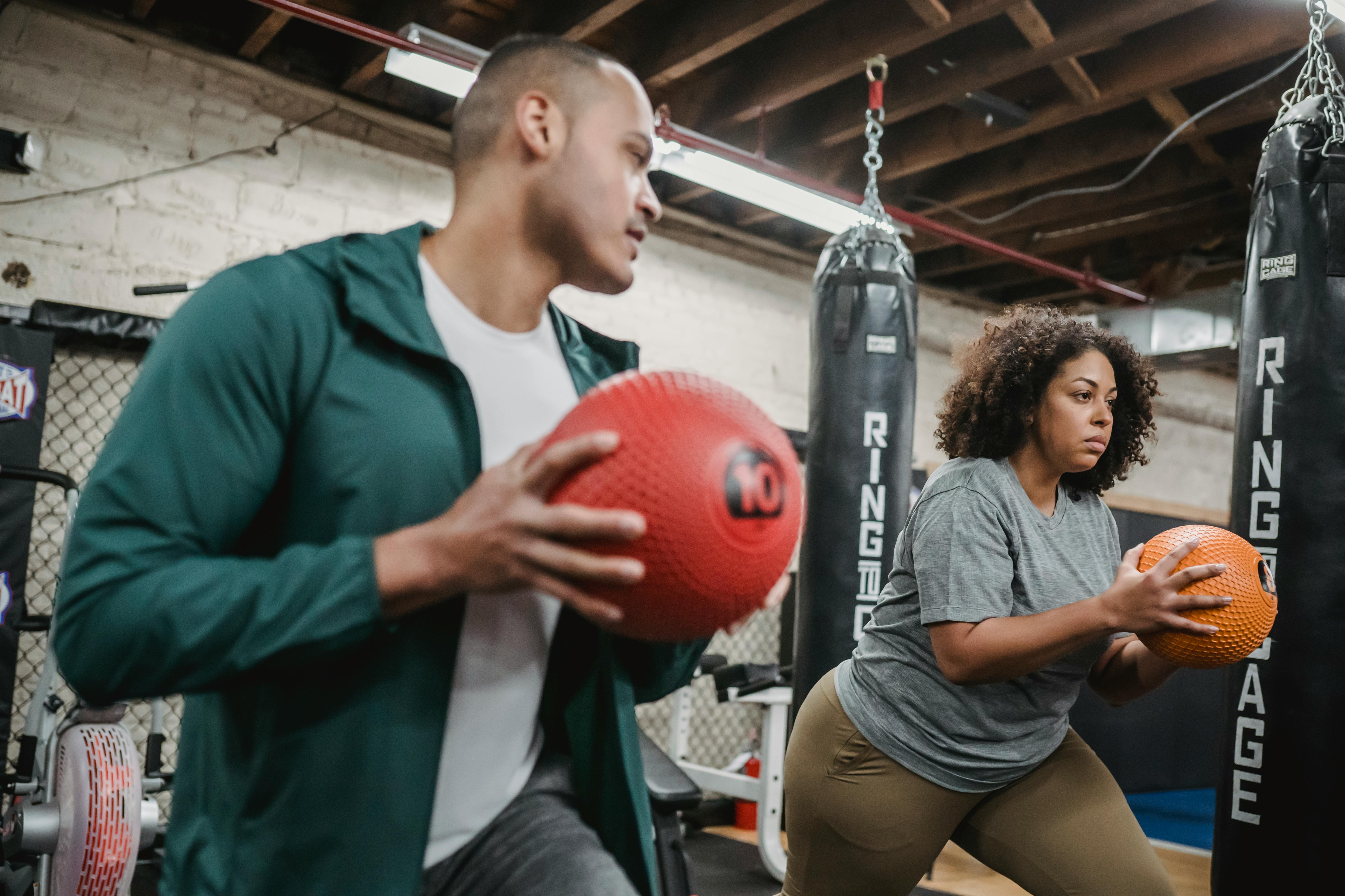 multiethnic young man and woman doing butt exercise with weigh balls in gym