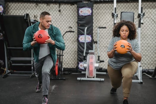 Two people engaging in a focused workout using medicine balls in an indoor gym setting.