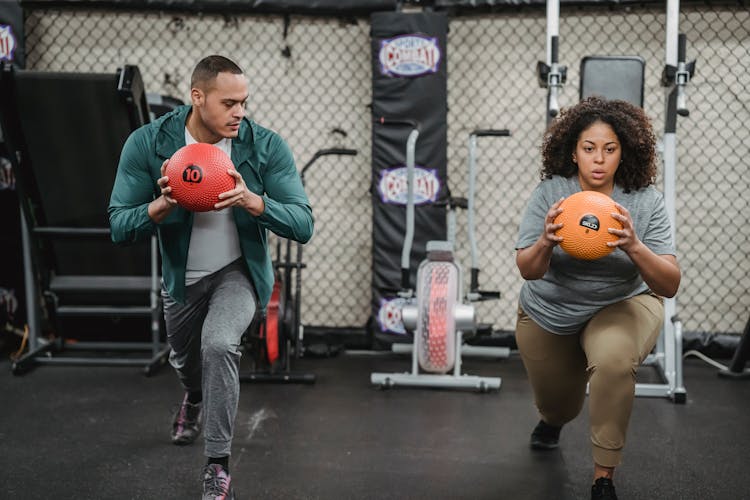 Multiethnic Fit Man And Obese Woman With Medicine Ball Doing Lunges In Sports Club