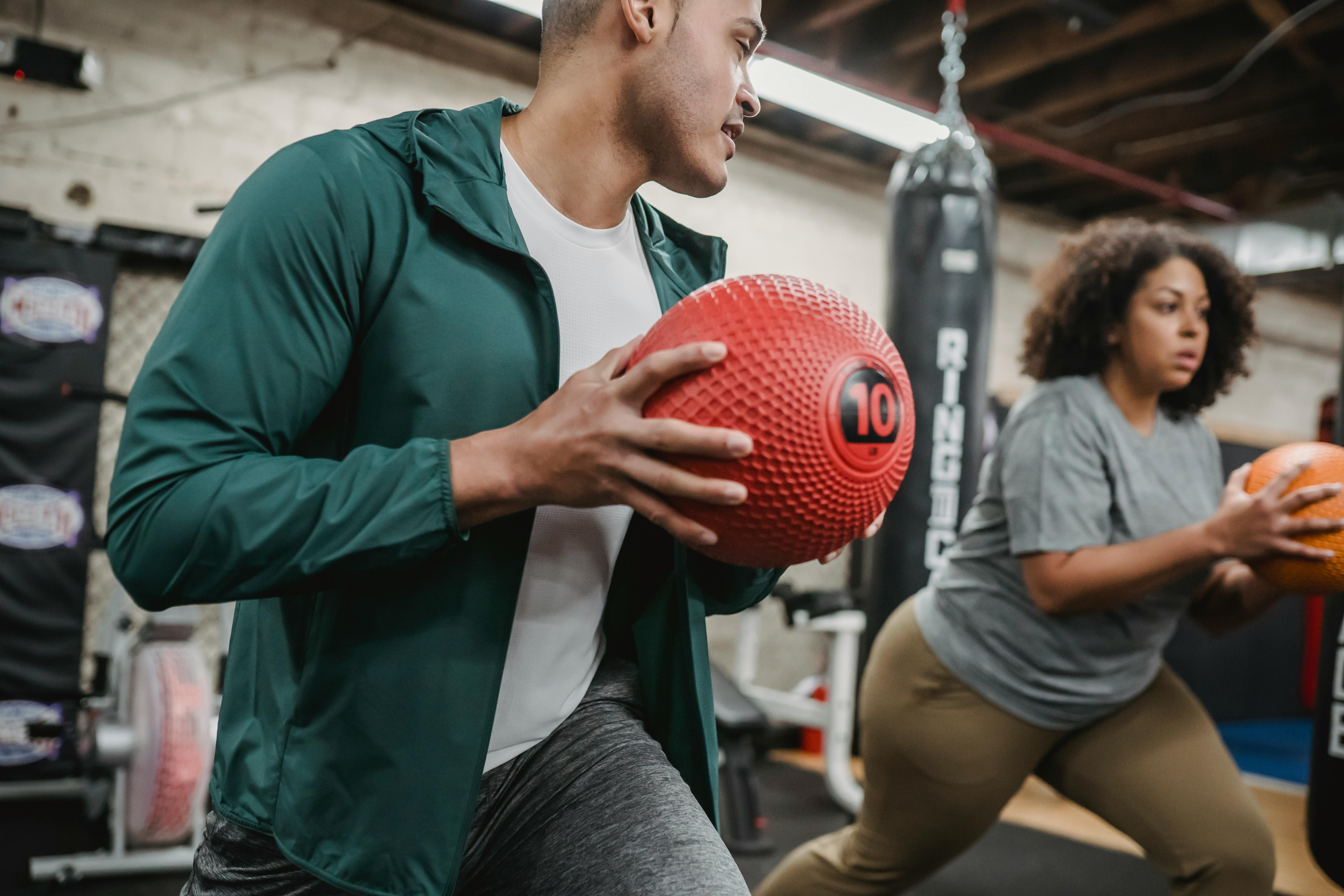 focused obese ethnic woman exercising with male instructor with medicine balls in hands