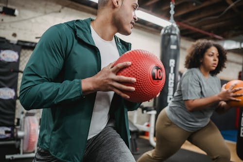 Focused obese ethnic woman exercising with male instructor with medicine balls in hands