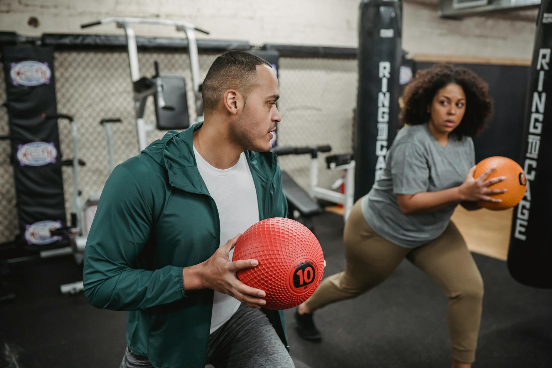 Two people engaged in a fitness routine with medicine balls in an indoor gym setting.