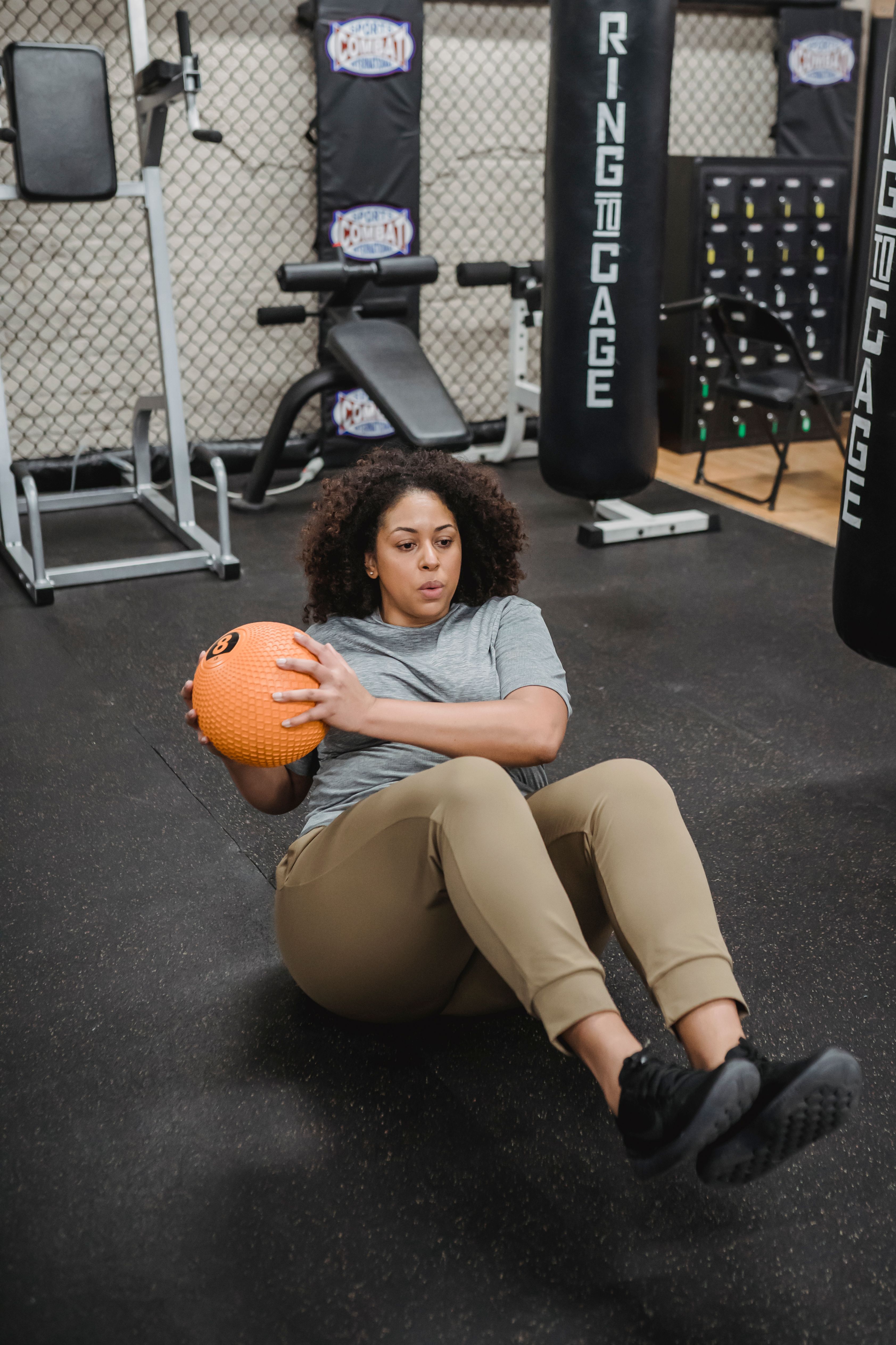 Full body of determined plump African American female warming up with ball in gym with modern equipment