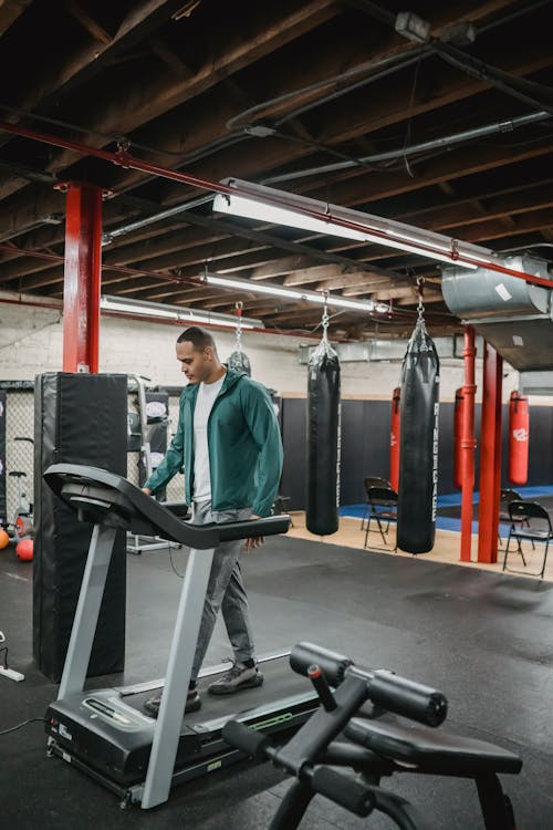 Full body of male in activewear on treadmill in sport club with punching bags