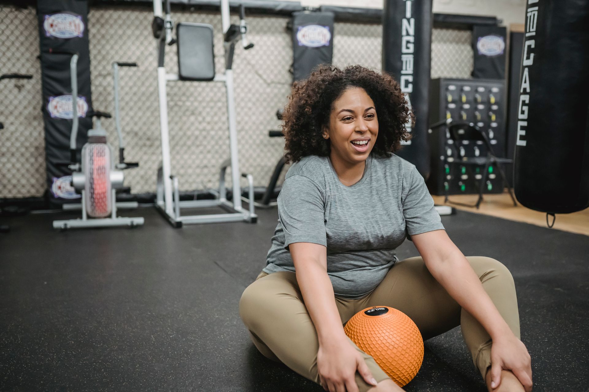 Happy plus size African American female smiling and warming up with ball in gym