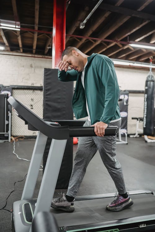Full body of exhausted male in activewear walking on treadmill in contemporary sport club