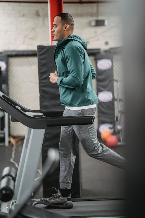 Pria Dengan Jaket Hijau Dan Celana Abu Abu Berdiri Di Treadmill Hitam