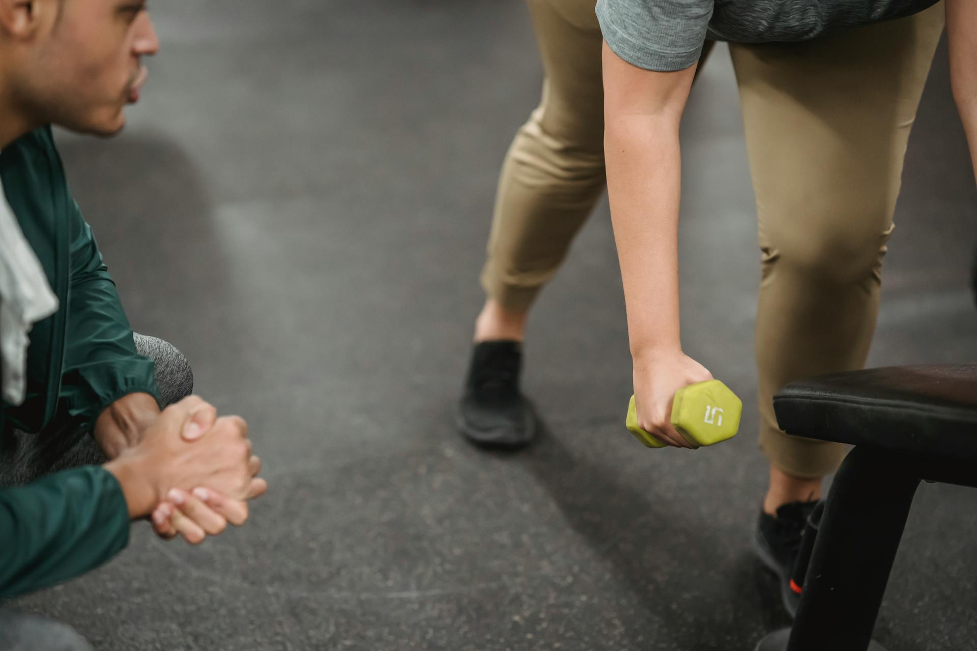 Instructor with hands clasped watching woman lifting dumbbell