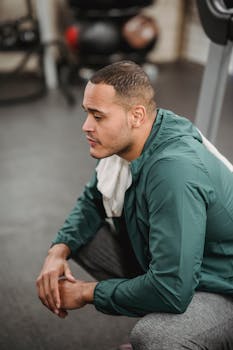 Side view of professional thoughtful coach in sportswear resting after working out on blurred background of gym