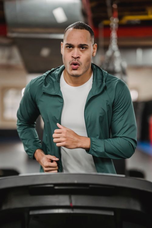 Free Serious male in sportswear jogging and breathing on modern treadmill on blurred background of gym Stock Photo