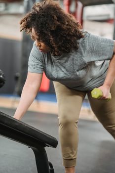 Crop African American female exercising with dumbbell while working out with gym equipment in sport club