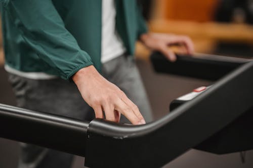 Crop anonymous male in activewear checking speed and time of treadmill on blurred background