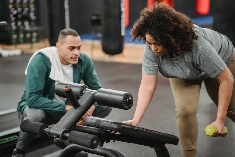 Sporty Trainer Supporting Black Woman Doing Exercises With Dumbbell