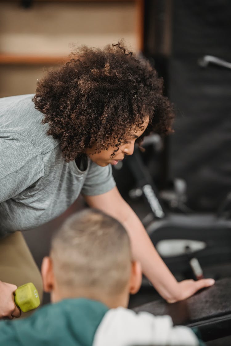 Diligent Black Woman Lifting Dumbbell While Trainer Supporting