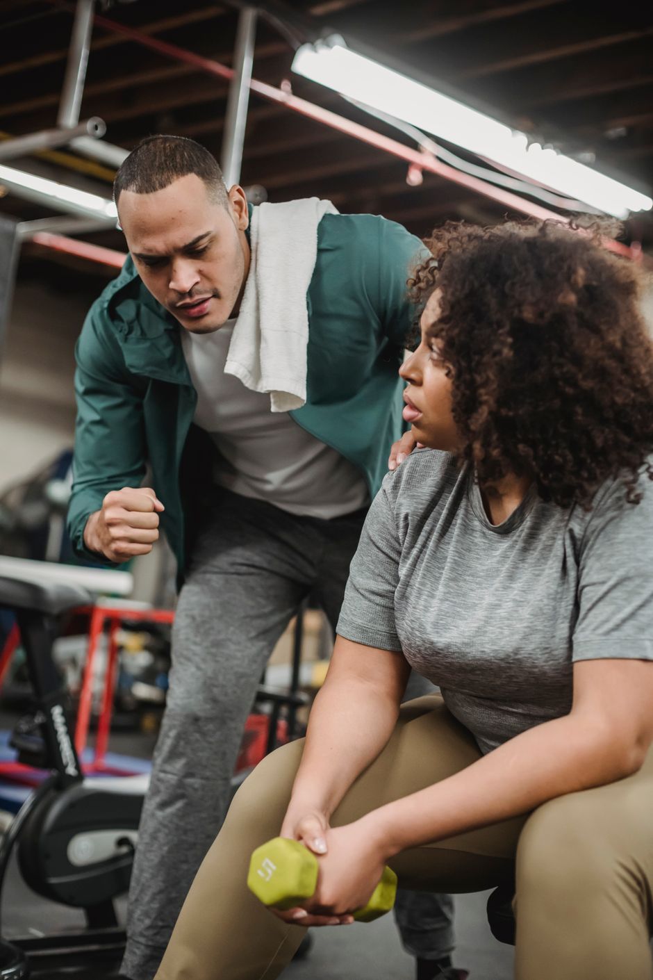 Head coach assisting a member with dumbbell form on the gym floor