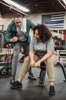 Personal trainer motivating client with dumbbell exercises in gym setting.