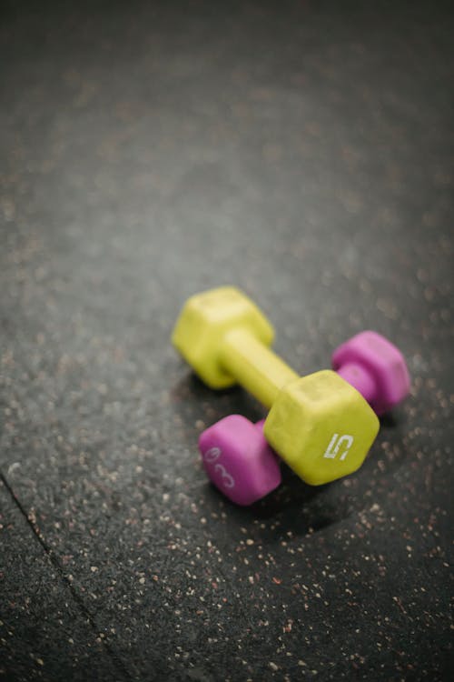 From above of multicolored fitness dumbbells placed on each other on dark gray surface