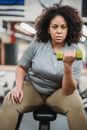 Overweight black woman lifting dumbbell in gym