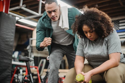 Free From below of strong personal coach explaining black woman how to exercise with dumbbells properly Stock Photo